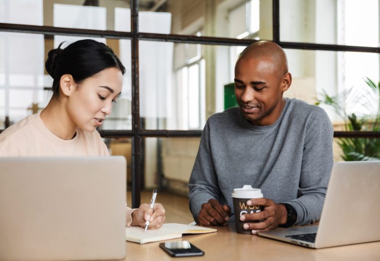 Image of multiethnic young female and male coworkers sitting at table and working on laptops in office